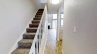 This two-story, 1-bedroom, 1-bathroom residence offers a well-organized layout that makes efficient use of its space across two levels. The main level welcomes you with warm hardwood-style flooring that extends through the open living area, where a fireplace serves as a focal point, creating a cozy and inviting atmosphere. Large windows with vertical blinds allow generous natural light to fill the space, enhancing the bright and airy feel of the interior. A functional kitchen with white cabinetry is conveniently positioned adjacent to the living area, offering a clean and practical workspace. A carpeted staircase with a white railing connects the two floors, providing a clean visual contrast between the levels. The textured ceilings and crisp white walls throughout contribute to a fresh, neutral palette that offers a versatile backdrop for any interior style. The upper level houses the private sleeping quarters, providing a comfortable retreat separated from the main living spaces. Overall, this residence combines practical design with comfortable living, making it an ideal space for those seeking a compact yet functional multi-level home.