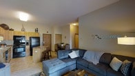 This single-floor residence offers a thoughtfully designed open-concept layout that seamlessly connects the main living areas. The living room serves as the heart of the space, featuring a large sectional sofa with plush seating, neutral-toned walls, and a relaxed, welcoming ambiance. Adjacent to the living area, the kitchen is equipped with warm yellow-toned cabinetry, a black refrigerator, and a granite-topped breakfast bar with stool seating — ideal for casual dining or entertaining. A separate dining area accommodates a full table and chairs, providing a dedicated space for meals. The entryway is clearly defined and leads naturally into the open living space. Interior doors provide access to additional rooms, maintaining a practical and efficient flow throughout. The flooring features light-toned tile in the main areas, contributing to a bright and airy atmosphere. The overall design balances functionality with comfort, making it a practical and livable single-floor home suitable for a range of lifestyles.