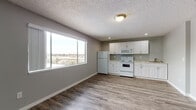 Located at 2136 West Riverside Avenue in Spokane, Washington, Unit 433 is a single-floor residence that combines functional design with clean, modern finishes throughout. The open-concept kitchen and living area serves as the heart of the unit, featuring durable wood-look flooring, neutral gray walls, and a textured ceiling. The kitchen is well-equipped with white cabinetry offering ample storage, light granite-style countertops, and a full suite of white appliances including a refrigerator, electric range, built-in microwave, and a sink. A large picture window in the kitchen and dining area frames a sweeping outdoor view of the Spokane landscape, flooding the space with natural light. The spacious living area provides an open, versatile layout with the same wood-look flooring carried throughout. The bathroom is thoughtfully appointed with a tub-shower combination, a white vanity with granite-style countertops, wood-look tile flooring, and a grab bar for added accessibility. Bedroom and closet areas are accessible via classic six-panel white interior doors, complemented by white trim and baseboards. The unit's cohesive color palette of soft grays and whites creates a calm, neutral ambiance suitable for a variety of living arrangements.