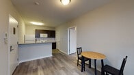 Located at 1718 N Sydenham St in Philadelphia, PA, this single-floor unit offers a clean, modern layout with consistent light gray luxury vinyl plank flooring throughout. The open-concept living and dining area connects seamlessly to a well-equipped kitchen, creating a practical and inviting common space. The kitchen features dark espresso cabinetry with brushed nickel hardware, granite-style countertops, a subway tile backsplash, and white appliances including a refrigerator, electric range, and over-the-range microwave. A peninsula with a granite countertop and sink serves as both a functional workspace and a casual dining divider. A compact dining area accommodates a small table and chairs, making efficient use of the available space. The bedroom is a comfortable, well-lit room with a window fitted with blinds that allow natural light to filter in, complemented by a wall-mounted HVAC unit for individual climate control. The bathroom features a light blue-gray accent wall, a dark vanity with granite countertop, a toilet, towel bars, and a walk-in shower with continuity of the vinyl plank flooring. The unit's neutral color palette and modern finishes throughout provide a clean, move-in-ready environment.