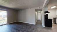 This single-floor residence offers a well-organized layout with a variety of thoughtfully finished spaces throughout. The main living area is open and spacious, featuring dark wood-style vinyl plank flooring and neutral gray walls that create a clean, modern aesthetic. A sliding glass door leads to a private balcony, allowing natural light to fill the room and providing views of the surrounding area. A textured popcorn ceiling is consistent throughout the main living spaces.

The galley-style kitchen is efficiently designed with white shaker cabinetry, granite-look countertops, a stainless steel sink, and black appliances including a refrigerator, range, and dishwasher. Open shelving adds additional storage and visual interest.

A dedicated hallway connects the living area to the private rooms. The bedrooms feature plush carpeting, neutral walls, and ample closet space with built-in shelving and hanging rods. One bedroom includes a window with natural light and exterior views.

The bathroom is finished with wood-style flooring, a full soaking tub with a shower surround, brushed nickel fixtures and grab bar, a toilet, and a granite-topped vanity. The overall palette remains cohesive and understated throughout the entire unit.