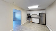 Located at 1445 Bodwell in Manchester, New Hampshire, this single-floor unit offers a thoughtfully laid-out living space with clean, updated finishes throughout. The kitchen is well-equipped with white shaker-style cabinetry, dark countertops, and a full suite of stainless steel appliances including a refrigerator, range, and over-the-range microwave. Light wood-tone vinyl plank flooring runs throughout the kitchen and connects seamlessly to the adjacent living areas. The open living and dining area is bright and welcoming, featuring neutral-toned walls, white baseboard trim, and durable wood-look flooring. A sliding glass closet and direct entry door provide practical convenience. The bedroom is a comfortable, well-proportioned room featuring a wall-mounted air conditioning unit, a baseboard heater, and a large window that invites natural light and outdoor views. The bathroom is neatly finished with a white vanity, dark stone-look countertop, a large mirror with overhead lighting, and a full tub and shower combination. Throughout the unit, textured ceilings, neutral wall tones, and consistent flooring choices create a cohesive, move-in-ready aesthetic that is both practical and inviting.