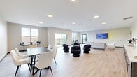 Located at 900 3rd St SE in Cedar Rapids, Iowa, this contemporary communal lounge offers a thoughtfully designed single-floor space ideal for gathering and socializing. The open-plan layout is anchored by light hardwood-style flooring that flows seamlessly throughout, complementing the neutral, warm-toned walls and recessed lighting overhead.

The room is organized into distinct yet connected zones. A cozy lounge area features a mix of plush upholstered sofas and accent chairs arranged around a low coffee table, creating an inviting setting for relaxed conversation. Adjacent to this is a more casual seating cluster with stylized curved chairs surrounding a gold accent table, adding a contemporary design flair. A dedicated dining and high-top bar table area provides additional flexible seating options.

A built-in wet bar with gray cabinetry, a sink, and counter space serves as a functional amenity along one wall, ideal for refreshments and casual entertaining. A wall-mounted display screen adds a modern, connected touch to the space.

Large windows and a sliding glass door open to an outdoor balcony, flooding the interior with natural light and offering elevated views of the Cedar Rapids skyline. The balcony extends the usable area and provides an appealing outdoor retreat. Clean lines, modern furnishings, and a well-considered layout make this space both functional and visually appealing.