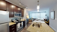 This well-designed single-floor residence offers a thoughtfully arranged open-concept layout that seamlessly connects the kitchen and living areas. The kitchen is a standout feature, showcasing rich dark espresso cabinetry, granite countertops, a central island with an undermount sink, and a full suite of stainless steel appliances including a refrigerator, electric range, built-in microwave, and dishwasher. Curved track lighting overhead adds a contemporary touch, while wood-look flooring runs throughout the main living areas for a warm, cohesive aesthetic. The living room is bright and welcoming, benefiting from expansive windows dressed with sheer curtains and horizontal blinds that allow abundant natural light to fill the space. The bedroom serves as a serene retreat, highlighted by a bold teal accent wall, plush carpeting, large windows with outdoor views, a sliding door to a private exterior space, and a sliding-door closet offering convenient storage. The bathroom continues the refined design language with a dark vanity, granite countertop, and well-lit mirror. Throughout the residence, neutral tones and modern finishes create a cohesive and contemporary living environment.
