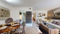 This thoughtfully designed single-floor residence offers a cohesive layout that maximizes every square foot. The combined living and dining area serves as the heart of the home, distinguished by a striking exposed brick accent wall that adds warmth and texture to the space. Large windows allow natural light to filter in through sheer curtains, creating an inviting ambiance. The living area features carpeted flooring, while the dining section transitions to rich hardwood-style flooring, providing a clear visual distinction between the two zones.

The kitchen is efficiently laid out with dark wood cabinetry, granite-style countertops, a double-basin stainless steel sink, and a dishwasher. An adjacent pantry provides additional storage. The bedroom is a comfortable retreat, featuring plush carpeting, a closet, and a window dressed with linen curtains that bathe the room in soft, natural light. A second closet adds to the overall storage capacity of the unit.

The bathroom is neatly appointed with a granite-style vanity countertop, a white sink basin, and hardwood-style flooring that mirrors the kitchen's aesthetic. Throughout the residence, a textured ceiling and clean white walls provide a neutral backdrop, allowing each room's individual character to shine.