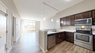 Located at 1520 Kenwood Ave in Duluth, MN, this one-bedroom, one-bathroom unit offers a well-designed, functional layout across a single floor. The open-concept kitchen and living area serves as the heart of the space, featuring rich dark-espresso cabinetry extending to the upper walls, granite-style countertops, a peninsula with bar seating, and a full suite of stainless steel appliances including a refrigerator, range, microwave, and dishwasher. Pendant lighting illuminates the kitchen, while hardwood-style plank flooring flows throughout the main living area, adding warmth and continuity. The living room is bright and airy, benefiting from large floor-to-ceiling windows that flood the space with natural light and offer views of the surrounding Duluth neighborhood. A private balcony extends the living space outdoors. The bedroom is a comfortable retreat finished with plush carpeting, neutral gray walls, and a generously sized window. The bathroom is clean and functional, featuring wood-look tile flooring, a dark-vanity cabinet, and a full tub-shower combination. A dedicated closet provides practical storage. The textured ceiling and track lighting throughout add to the unit's modern, polished character.