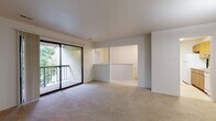 This single-floor, two-bedroom, one-bathroom unit offers a functional and comfortable layout with a neutral color palette and carpeted living areas throughout. The spacious living room serves as the heart of the home, featuring sliding glass doors that open to a private balcony with a railing, allowing natural light to fill the space and providing pleasant outdoor views of surrounding trees.

The galley-style kitchen is efficiently designed with warm oak cabinetry lining both sides, light countertops, tile flooring, and white appliances including an electric range and refrigerator. A pass-through opening connects the kitchen to the living area, enhancing the open feel of the shared spaces.

Both bedrooms are carpeted and well-sized, each featuring windows with leafy tree views that bring in natural light and a sense of tranquility. The primary bedroom includes a ceiling fan with light fixture. The second bedroom offers additional versatility for use as a guest room or home office.

The full bathroom features tile flooring, a wood-toned vanity with ample cabinet storage, a wall mirror, and a tub-shower combination. A dedicated laundry area houses a stacked washer and dryer unit alongside a water heater, adding everyday convenience to the space.