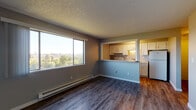 Located at 2136 West Riverside Avenue in Spokane, WA, this single-floor residence offers a thoughtfully laid-out living space with consistent wood-look flooring throughout. The open living area is a standout, anchored by a large picture window that frames sweeping views of the Spokane cityscape and surrounding greenery, filling the room with abundant natural light. A baseboard heating system runs along the perimeter, ensuring comfort year-round. The kitchen connects to the living area via a convenient pass-through counter, and features white cabinetry, granite-style countertops, a stainless steel sink, and a full-size refrigerator — providing a functional and clean aesthetic. The bedrooms are well-sized, each featuring wood-look flooring, baseboard heating, and closet storage, with one bedroom offering a sliding-door closet and scenic outdoor views. Additional rooms include a versatile space with track lighting, neutral gray walls, and its own closet — suitable as a bedroom or flexible-use room. The bathroom is finished with classic white tile surrounding a full soaking tub. Textured ceilings and neutral tones throughout give the space a clean, move-in ready feel well-suited for comfortable everyday living.