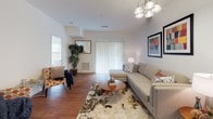 Located at 10 Connors Ave in Mansfield, Massachusetts, this single-floor residence offers a thoughtfully designed layout with contemporary finishes throughout. Rich hardwood flooring flows seamlessly across the main living areas, complementing the clean, bright white walls that create an open and welcoming atmosphere.

The living room is generously proportioned, featuring a chandelier overhead, a sliding glass door that invites natural light, and ample space for comfortable seating arrangements. The kitchen is well-equipped with white shaker-style cabinetry, gray countertops, and a full suite of stainless steel appliances including a range, microwave, dishwasher, and refrigerator, all set atop warm hardwood flooring.

The bedroom is a serene retreat, offering notable ceiling height, natural light from a double window, and warm hardwood floors. A spacious walk-in closet with wire shelving provides generous storage. The bathroom features tile flooring, a vanity with a marble-style countertop, and a shower with tub.

A dedicated laundry room houses a full-size washer and dryer side by side, adding everyday convenience. A bright hallway connects the rooms, enhancing the home's functional flow. Overall, this residence combines practical amenities with clean, modern design.