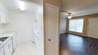 This single-floor residence offers a practical and well-organized layout designed for comfortable everyday living. The kitchen is finished with light ceramic tile flooring and outfitted with white cabinetry, a full-size refrigerator, a stove, and a dishwasher, creating a clean and efficient workspace. Upper cabinets provide ample storage, and the bright white finishes give the kitchen a fresh, airy feel. Adjacent to the kitchen, a closet or utility door offers additional storage convenience. The living area transitions seamlessly from the kitchen space and features rich, dark hardwood-style flooring that adds warmth and contrast to the neutral beige walls. A ceiling fan with a light fixture overhead provides both air circulation and ambient lighting, while a window dressed with horizontal blinds allows natural light to fill the room and offers views to the outdoors. The warm, neutral color palette used throughout the residence creates a cohesive and inviting atmosphere. The combination of tile in the kitchen and hardwood-style flooring in the living area provides both practicality and aesthetic appeal, making this a well-balanced and move-in-ready space.