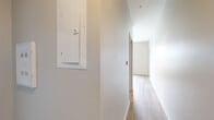 This well-appointed single-floor space offers a clean, modern aesthetic defined by neutral walls, light wood-tone flooring, and an open, airy layout. The kitchen serves as a functional centerpiece, outfitted with rich dark-stained cabinetry, light countertops, and a full suite of stainless steel appliances including a refrigerator, range, over-the-range microwave, and dishwasher. Recessed lighting illuminates the kitchen area, which flows seamlessly into the adjacent living space. A sliding barn-style door adds a stylish architectural accent near the entryway. The hallway, featuring an accessible electrical panel and smoke detector, connects the main living areas to the private rooms. The bedrooms are bright and inviting, each benefiting from natural light admitted through large windows fitted with horizontal blinds. The bathroom is cleanly finished with a granite-topped dark wood vanity, a framed mirror, grab bars for accessibility, and wood-look flooring that ties cohesively to the rest of the unit. Throughout the space, consistent use of light flooring, white trim, and neutral wall tones creates a cohesive and contemporary atmosphere that is both functional and move-in ready.