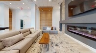 Located on Old Trail Drive in Crozet, VA, this single-story amenity space combines modern design with thoughtfully curated gathering areas. The open-concept kitchen features dark flat-front cabinetry, a large white quartz island with bar seating, stainless steel appliances, open shelving, and dramatic cascading pendant lighting. Tall windows at the far end flood the space with natural light and provide outdoor views.

Multiple lounge areas offer distinct atmospheres. One features soaring ceilings, floor-to-ceiling windows, tufted caramel leather sofas, and a marble-top coffee table. Another centers around a bold dark accent wall with a linear fireplace flanked by stacked wood detail and a mounted television. A third lounge incorporates a slatted wood accent wall, a live-edge coffee table, and an additional linear fireplace with stacked stone surround.

A dedicated game room showcases a full poker table beneath an industrial pendant light, complemented by a warm cedar wood accent wall with a mounted display. Exposed wood ceiling beams and a sliding barn door add rustic character to the casual dining and lounge area nearby.

The fitness center is well-equipped with Life Fitness cardio machines, free weights, mirrors, and generous natural light from large windows overlooking an exterior terrace and stone facade exterior.
