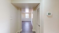 Located at 7016 Park Heights Ave in Baltimore, MD, this single-floor unit offers a clean, updated interior with a practical and straightforward layout. The living area features light gray luxury vinyl plank flooring that extends throughout the main living spaces, complemented by crisp white walls and bright, neutral tones that create an open and airy atmosphere. Natural light filters in through multiple windows fitted with blinds, providing views of the surrounding neighborhood.

The kitchen is equipped with light wood cabinetry offering generous storage, dark laminate countertops, and black appliances including a refrigerator, dishwasher, and a stainless steel range. Tile flooring adds durability to this functional cooking space.

The bedroom is carpeted for comfort and benefits from two windows that bring in ample natural light, adding to the room's welcoming feel. A hallway with a louvered-door closet provides convenient storage and connects the living spaces efficiently.

The bathroom features classic white square wall tiles accented with dark and blue tile trim, a combined tub and shower, a toilet, and a vanity. A window above the tub allows for natural ventilation. Overall, this unit presents a well-maintained, move-in ready space with consistent finishes throughout.