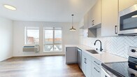 Located in the vibrant Uptown neighborhood of Minneapolis, this one-bedroom, one-bathroom unit offers a thoughtfully designed open-concept layout with modern finishes throughout. Warm hardwood-style flooring flows seamlessly across the entire living space, creating a cohesive and inviting atmosphere.

The kitchen is a standout feature, showcasing gray flat-front cabinetry with matte black hardware, a herringbone-patterned tile backsplash, light quartz countertops, and a full suite of stainless steel appliances including a refrigerator, range, microwave, and dishwasher. A stylish pendant light anchors the kitchen area, which opens directly into the living space. Large windows flood the combined kitchen and living area with natural light and provide views of the surrounding neighborhood rooftops.

The bedroom is a cozy, well-proportioned room with the same hardwood-style flooring and clean white walls. A sliding barn-style door leads to a dedicated walk-in closet with built-in shelving, offering practical storage solutions.

The bathroom features a full tub-shower combo with matte black fixtures, complemented by a light vanity with a marble-style countertop and an accent wall in a deep slate blue, adding a touch of character. A connecting hallway ties the rooms together efficiently, completing this well-appointed urban residence.