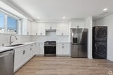 Located at 1297 1/2 W 36th St in Los Angeles, this modern three-story home offers seven bedrooms and seven bathrooms across three thoughtfully laid-out floors. The ground floor is the largest and serves as the communal hub, featuring an open-concept kitchen, dining room, and living room. The kitchen is outfitted with white shaker cabinetry, white subway tile backsplash, stainless steel appliances including a gas range and two full-sized refrigerators, and recessed lighting throughout. The adjacent dining area comfortably seats a large group and is bathed in natural light from wide windows. A cozy living room with a sectional sofa completes the shared space. Stainless steel stacked washer and dryer units are also conveniently located on this level. The upper two floors house the seven bedrooms, each bright and minimally styled with light wood-look flooring, recessed lighting, and windows offering neighborhood views. Bedrooms include desks, making them well-suited for focused work or study. The seven bathrooms are clean and contemporary, featuring white vanities with illuminated mirrors, and select bathrooms include a tub-shower combo with floor-to-ceiling white tile. A striking angled stairwell with clean white walls connects the floors, adding an architectural element to the interior.
