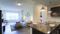 Located at 1 Parker Ave in the Manayunk neighborhood of Philadelphia, PA, this single-floor residence offers a thoughtfully designed open-concept layout that connects the kitchen, dining, and living areas into one cohesive living space. The kitchen features dark granite countertops with a breakfast bar overhang, a stainless steel sink, and an industrial-style pendant light that adds a modern touch. The open bar-height counter flows naturally into the dining area, making it an ideal space for both casual meals and entertaining. The living room is bright and inviting, with light-toned walls, rich hardwood flooring, and a large window that allows natural light to fill the space. A plush sofa, coordinating accent furniture, and a patterned area rug create a warm and comfortable atmosphere. A partial wall divides the living space from the hallway, which leads to the bedroom visible in the background. The bedroom benefits from the same clean, neutral palette that defines the rest of the home. Overall, the residence combines contemporary finishes with a cozy, well-organized layout, making it a functional and aesthetically pleasing living environment in one of Philadelphia's most vibrant neighborhoods.