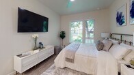 This thoughtfully designed single-floor unit offers a cohesive blend of modern aesthetics and functional living. The bedroom is a bright, serene retreat featuring large windows that frame lush green tree views, filling the room with natural light. Light wood-style flooring runs throughout, complemented by neutral wall tones that create a calm, inviting atmosphere. A wall-mounted flat-screen TV and ceiling fan add practical comfort to the space.

The kitchen is offered in two configurations visible across the unit variations: a galley-style layout with crisp white cabinetry, quartz countertops, stainless steel appliances — including a refrigerator, range, and microwave — and a deep undermount sink; and an open kitchen with a peninsula breakfast bar illuminated by pendant lighting, ideal for casual dining and entertaining. Both layouts feature light wood-style flooring and abundant upper and lower cabinet storage.

The bathroom is clean and contemporary, outfitted with a white vanity, quartz countertop, undermount sink with a modern faucet, and a mirrored medicine cabinet above. A shower-tub combination with a curtain, wood-style flooring, and warm neutral walls round out the space with understated elegance. Together, these spaces deliver a polished, move-in-ready living environment.