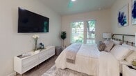 This thoughtfully designed single-floor unit offers a cohesive blend of modern aesthetics and functional living. The bedroom is a bright, serene retreat featuring large windows that frame lush green tree views, filling the room with natural light. Light wood-style flooring runs throughout, complemented by neutral wall tones that create a calm, inviting atmosphere. A wall-mounted flat-screen TV and ceiling fan add practical comfort to the space.

The kitchen is offered in two configurations visible across the unit variations: a galley-style layout with crisp white cabinetry, quartz countertops, stainless steel appliances — including a refrigerator, range, and microwave — and a deep undermount sink; and an open kitchen with a peninsula breakfast bar illuminated by pendant lighting, ideal for casual dining and entertaining. Both layouts feature light wood-style flooring and abundant upper and lower cabinet storage.

The bathroom is clean and contemporary, outfitted with a white vanity, quartz countertop, undermount sink with a modern faucet, and a mirrored medicine cabinet above. A shower-tub combination with a curtain, wood-style flooring, and warm neutral walls round out the space with understated elegance. Together, these spaces deliver a polished, move-in-ready living environment.