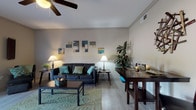 This single-floor, 1-bedroom, 1-bathroom residence offers a thoughtfully designed layout that maximizes comfort and functionality throughout. The living room serves as the heart of the home, featuring light wood-look flooring, crown molding, and a ceiling fan overhead. A sliding glass door floods the space with natural light and provides direct access to a green outdoor area, enhancing the open and airy feel of the room. Adjacent to the living area, a dedicated dining space accommodates a dark wood table and chairs beneath decorative wall art, creating an intimate setting for meals. The kitchen is well-equipped with dark espresso cabinetry, granite-style countertops, a double stainless steel sink, and ample upper and lower storage — all tied together with coordinating light flooring. The bedroom is a serene retreat, highlighted by a large window with outdoor views, light hardwood-style flooring, and generous space for furniture. The full bathroom features tile flooring and a shower/tub combination, accessed conveniently from the hallway. Throughout the residence, neutral wall tones and consistent flooring create a cohesive, modern aesthetic that is both practical and visually appealing.