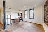 Located in the heart of New Orleans' Central Business District, this 2-bedroom, 1-bathroom unit at 234 Loyola Ave blends industrial character with modern finishes across a single floor. The open-plan living, dining, and kitchen area serves as the heart of the home, anchored by a ceiling fan, large double-hung windows that flood the space with natural light, and a distinctive exposed steel column that speaks to the building's architectural heritage. The kitchen is outfitted with stainless steel appliances, including a refrigerator, dishwasher, microwave, and range, complemented by warm wood cabinetry. Concrete floors run throughout, adding to the loft-inspired aesthetic. The primary bedroom is a standout space, featuring dramatic exposed brick walls and large windows with sweeping views of the New Orleans skyline. The second bedroom is bright and well-proportioned, also benefiting from generous window placement and city views. A hallway connects the bedrooms and provides access to four closets, offering ample storage. The full bathroom is finished with gray subway tile in the tub/shower surround, coordinating floor tile, a wood vanity, and a white quartz countertop. The overall ambiance is modern-industrial, well-suited to urban living in a vibrant downtown location.
