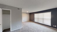 Located at 4216 Garrett Rd in Durham, NC, this single-floor unit offers a well-organized layout with a practical and modern interior design. The living area is generously sized, featuring plush wall-to-wall carpeting and a distinctive two-tone color scheme, with a bold dark accent wall paired with lighter neutral tones. A large window fitted with horizontal blinds allows natural light to fill the space, while a textured ceiling adds dimension overhead. The kitchen is efficiently designed with wood-look flooring, crisp white cabinetry, granite-style countertops, and a full suite of stainless steel appliances, including a range, over-the-range microwave, and refrigerator. A pass-through window connects the kitchen to the adjacent living area, enhancing the open feel of the layout. The bedrooms continue the carpeted, neutral aesthetic with soft gray walls, clean white trim, and ample room for a variety of furniture arrangements. The bathroom features a full tub and shower combination with a bright white surround and chrome fixtures, maintaining the clean, functional character found throughout the unit. Overall, the space presents a cohesive, move-in ready environment with consistent finishes throughout.