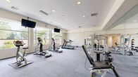Located at 31220 Samantha Ln in Temecula, CA, this well-appointed fitness center offers a single, generously sized exercise room designed to support a comprehensive workout experience. The space is bathed in natural light, thanks to a large bank of floor-to-ceiling windows along one wall that frame views of surrounding greenery, creating an inviting and energizing atmosphere.

The exercise room is thoughtfully equipped with a wide range of cardio machines, including treadmills, elliptical trainers, and a stationary bike, all positioned to take advantage of the natural light and outdoor views. A dedicated strength-training area features multiple cable and weight machines, along with a dumbbell rack, catering to a full range of resistance workouts.

Full-length mirrors line one wall, visually expanding the space while allowing users to monitor their form during exercise. Overhead, recessed lighting supplements the abundant natural light, ensuring consistent illumination throughout the room. Wall-mounted flat-screen televisions are strategically placed for viewing during cardio sessions. The floor is finished with durable, patterned carpet tiles that provide comfort and traction underfoot. The neutral color palette of the walls and ceiling contributes to a clean, modern aesthetic that keeps the focus on fitness.