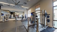 Located at 451 2nd Ave S in Saint Petersburg, Florida, this single-floor fitness center is designed to accommodate a comprehensive range of workout disciplines. The space is organized into distinct functional zones that flow seamlessly into one another, creating an efficient and motivating training environment.

The cardio area is lined with large windows fitted with roller shades, allowing abundant natural light to filter in while offering views of an outdoor area. Treadmills, ellipticals, and stair climbers are arranged along this windowed wall, with mounted flat-screen TVs positioned for viewing during workouts. A large ceiling fan overhead enhances air circulation throughout the main floor.

The strength training section features a power rack, cable machines, a full dumbbell rack, kettlebells, and medicine balls, all set on durable rubber flooring with interlocking mat sections for added safety. Full-length mirrors line portions of the walls, visually expanding the space and supporting form monitoring during lifts.

A dedicated functional training and stretching zone occupies a separate area, distinguished by dark accent walls and rubber mat flooring. This section includes a heavy bag, TRX suspension system, stability balls, and open floor space for bodyweight or mat-based exercises. An adjacent glass-door room with vibrant orange accent walls provides a private studio space.