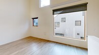 Located at 2730 N Killingsworth St in Portland, Oregon, this two-story residence offers a thoughtfully designed layout across two floors. The entry level is compact, leading to a carpeted staircase with clean white walls and a sleek metal handrail that draws the eye upward toward natural light above.

The main living floor hosts the majority of the space, where light hardwood-style flooring runs throughout, lending warmth and continuity to the open-plan layout. The kitchen is efficiently arranged with white cabinetry, under-cabinet lighting, a stainless steel sink, an electric range, built-in microwave, and a full-size refrigerator. A pendant light fixture accents the adjacent dining area, which flows seamlessly into the living room. The living room is a standout feature, boasting soaring ceilings, large floor-to-ceiling windows, and a clerestory window that floods the space with natural light and provides views of the surrounding neighborhood.

The bedroom features light hardwood flooring, vaulted ceiling angles, and a ceiling fan, creating a comfortable and airy retreat. The bathroom is clean and functional, finished with neutral tones, tile flooring, a walk-in shower with white subway tile surround, and a vanity with ample counter space. The overall ambiance is modern, minimal, and bright.