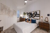 Located at 9330 Main St in Houston, TX, this single-floor residence offers a thoughtfully designed layout with modern finishes throughout. The kitchen is a standout feature, outfitted with sleek flat-front cabinetry in a soft gray tone, a classic white subway tile backsplash, granite countertops, and a full suite of stainless steel appliances including a range, microwave, and French door refrigerator. Light wood-style flooring flows through the main living areas, adding warmth and continuity to the space. The living area is bright and welcoming, featuring large sliding glass doors that open to a private balcony with outdoor seating and views of lush greenery below. The primary bedroom is generously proportioned with soaring ceilings that enhance the sense of openness, while a secondary bedroom offers plush carpeting, a natural window, and ample wall space. The primary bathroom is well-appointed with a dual-sink vanity topped with granite, a wide mirror with vanity lighting, and wood-style flooring that mirrors the main living areas. Throughout, the residence maintains a clean, contemporary aesthetic defined by white walls, recessed lighting, and an overall bright and airy ambiance suited to modern urban living.