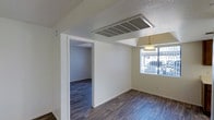 This single-floor space offers a clean, functional layout designed to maximize everyday livability. The interior is finished with rich, dark hardwood-style flooring that runs consistently throughout, providing a warm and cohesive aesthetic across all visible areas. Walls are painted in a crisp, neutral white, creating a bright and inviting atmosphere that complements the natural light filtering in through the windows.

The dining area is highlighted by a classic pendant light fixture that hangs overhead, adding a subtle decorative touch to the space. A large window allows natural light to fill the room, contributing to an open and airy feel. The textured ceiling adds a layer of architectural character throughout.

A central HVAC vent is prominently integrated into the ceiling, ensuring efficient climate control across the unit. An open doorway connects the main living and dining areas to an adjacent room, maintaining a sense of flow and continuity throughout the floor plan.

Overall, this space presents a straightforward and well-maintained interior, well-suited for comfortable day-to-day living. The neutral palette and consistent flooring create a versatile backdrop ready for personalization.