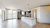 This single-floor residence at 301 Axis Dr in Louisville, KY offers a well-designed open-concept layout with contemporary finishes throughout. The kitchen serves as a central feature, showcasing dark espresso cabinetry, light quartz countertops, a mosaic tile backsplash, and a full suite of stainless steel appliances including a refrigerator, range, dishwasher, and built-in microwave. A built-in wine rack adds a distinctive detail above the cabinetry. A large white island with a clean quartz surface anchors the open living area, which features light wood-style flooring that flows throughout the main spaces. Natural light enters generously through large windows fitted with horizontal blinds. The bedroom is carpeted and benefits from an oversized window with outdoor views, while an adjacent walk-in closet provides extensive wire shelving and hanging space along multiple walls. The primary bathroom includes a marble-tiled walk-in shower with frameless glass doors and polished chrome fixtures, alongside a separate soaking tub and wood-look tile flooring. A dedicated laundry room houses a side-by-side full-size washer and dryer. The overall ambiance is clean, modern, and functional.