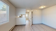 Located at 1445 SW A St in Corvallis, Oregon, Unit 7 is a thoughtfully laid-out single-floor residence with a bright, neutral palette throughout. The main living area features light wood-style flooring, a textured ceiling, and a large window fitted with horizontal blinds that allows natural light to fill the space. Baseboard heating runs along the perimeter, ensuring consistent warmth. The living area flows openly toward a half-wall partition that separates it from the kitchen. The kitchen is efficiently designed with white cabinetry, ample counter space, a stainless steel sink beneath a window, an electric coil range, and a full-size refrigerator — all finished in white for a clean, cohesive look. A hallway connects the living and kitchen areas to the rest of the unit. The bedroom is carpeted for added comfort and includes a window with blinds, baseboard heating, and access to a closet. The bathroom features light wood-style flooring consistent with the main living areas, a white vanity with storage, and a toilet, all presented in a clean and functional layout. Throughout the unit, the design is simple and practical, with white walls and understated finishes creating a bright, move-in-ready environment.