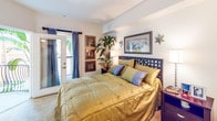 Located in the heart of Los Angeles at 1221 W Third St, this single-floor residence offers a thoughtfully designed layout with a refined aesthetic throughout. The open-concept living and dining area serves as the centerpiece of the home, featuring crown molding, plush carpeting, and large sliding glass doors that frame views of a private balcony with wrought iron railings and lush palm tree surroundings, flooding the space with natural light. The living room accommodates comfortable seating alongside elegant drapery and track lighting, creating a warm and inviting atmosphere. Adjacent to the dining area, the kitchen is outfitted with light wood cabinetry, granite-style countertops, a double stainless steel sink, a dishwasher, and a full refrigerator, all set against striking deep teal accent walls that add a bold design element. The bedroom is a serene retreat with soft carpeting, direct balcony access through glass French doors, and ample space for a full dresser and storage. The full bathroom features tile flooring, warm wood vanity cabinetry with dark stone countertops, a soaking tub with shower, and textured wallcovering that lends a spa-like quality. Throughout the residence, the design balances comfort and style with carefully curated finishes.