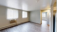 Located at 2920 W Highland Blvd in Milwaukee, WI, this single-floor, 3-bedroom, 1-bathroom unit offers a practical and well-organized layout. Hardwood-style flooring runs consistently throughout the space, providing a cohesive and clean aesthetic. The living room is a comfortable, open area featuring multiple windows dressed with vertical blinds that allow generous natural light, along with a wall-mounted air conditioning unit and baseboard heating. Adjacent to the living room, the kitchen is efficiently designed with white shaker-style cabinetry, light countertops, a gas range, and a full-size refrigerator — offering ample storage and functionality. The three bedrooms each feature hardwood-style flooring, vertical blinds, natural light from windows, and baseboard heating. The primary bedroom includes a built-in double closet, providing strong storage capacity. A hallway with louvered closet doors connects the rooms seamlessly. The full bathroom is clean and bright, featuring a white vanity with cabinet storage, a tub/shower combination with white tile surround, and wood-style flooring. Neutral light-gray wall tones throughout create a calm, move-in-ready atmosphere suited for everyday living.