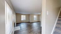Located at 14A Merry Ln in Greenville, NC, this two-story home offers three bedrooms and three bathrooms across two well-proportioned floors. The main level features a generous living room with rich, dark hardwood-style flooring, neutral beige walls, and multiple windows that invite an abundance of natural light. A classic fireplace with a tile surround serves as a focal point, adding warmth and character to the space. The kitchen is equipped with warm oak cabinetry, light countertops, and white appliances including a range, dishwasher, and refrigerator, all set atop matching hardwood-style flooring. A second living area on the main floor provides additional flexible space. Upstairs, the three bedrooms are finished with plush carpet and feature ample closet storage, including dedicated closets in each room. The spacious primary bedroom offers generous proportions and natural light. The three bathrooms are clean and functional, with one featuring a wood-toned vanity with storage and a lighted mirror. Bathtub and shower combinations complete the upper-floor bathrooms. Outside, the property is framed by tall, mature pine trees, offering a serene and private wooded setting with open green space — a standout feature of this Greenville home.