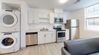 Located at 815 S Aurora St in Ithaca, NY, this compact and efficiently designed 2-bedroom, 1-bathroom unit offers a clean, modern aesthetic throughout. The open-concept living and kitchen area is bright and welcoming, with multiple windows that allow natural light to fill the space and offer views of surrounding greenery. Light wood-tone flooring runs through the main living area, contributing to the unit's fresh, contemporary feel.

The kitchen is well-appointed with white shaker-style cabinetry, light countertops, and a full suite of stainless steel appliances — including a refrigerator, electric range, over-the-range microwave, and dishwasher. A stacked washer and dryer unit is conveniently integrated into the kitchen area, adding practical in-unit laundry access.

Each bedroom features carpeted flooring, a desk and chair, and windows with views of the wooded surroundings, providing a quiet and functional space for rest or study. The bedrooms are cozy and well-suited for focused living.

The bathroom is finished in a clean, minimal style with light wood-tone flooring, a white vanity with storage, a wall mirror, and a full soaking tub with shower. The all-white walls and fixtures give the bathroom a bright, tidy appearance. Overall, this unit combines modern finishes with practical functionality in a well-located Ithaca setting.