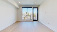Located at 806 N Edinburgh Ave, Unit 506 in Los Angeles, CA 90046, this modern 2-bedroom, 2-bathroom condominium offers 980 square feet of thoughtfully designed living space in the heart of West Hollywood. Light-toned hardwood flooring runs throughout, complementing the clean white walls and minimalist aesthetic that define the unit.

The open-concept kitchen and living area features flat-panel cabinetry in a warm wood finish, white quartz countertops, a tiled backsplash, and a full suite of stainless steel appliances including a refrigerator, range, and dishwasher. The living area connects seamlessly to a private balcony through floor-to-ceiling sliding glass doors, offering treetop and neighborhood views.

The primary bedroom spans 200 square feet and is bathed in natural light through large corner windows framing lush outdoor greenery. It features a wall of built-in floor-to-ceiling cabinetry with sleek black hardware for ample storage. The second bedroom also enjoys generous natural light via large black-framed windows with open sky views.

Both bathrooms are finished in a contemporary style with light wood vanities, white countertops, frameless glass walk-in showers with built-in benches, and large-format tile flooring, creating a clean, spa-like atmosphere throughout.