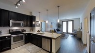 This 2-bedroom, 2-bathroom residence delivers a well-balanced blend of modern design and functional living. The open-concept floor plan creates a seamless flow between the kitchen, dining, and living areas, making the space feel expansive and connected. The kitchen is a standout feature, showcasing rich dark cabinetry that contrasts elegantly with light stone countertops. A peninsula island with a stainless steel sink serves as both a prep space and a casual gathering point, while stainless steel appliances — including a range and dishwasher — complete the chef-friendly setup. Pendant lighting above the island adds warmth and a contemporary touch. The living area extends naturally from the kitchen, featuring durable hardwood-style flooring that runs throughout the main living space. Large French doors invite natural light deep into the interior and provide a direct connection to the outdoors. Neutral wall tones and clean architectural lines create a calm, modern ambiance throughout. The overall layout is practical and polished, offering comfortable accommodations across two bedrooms and two full bathrooms, making it an ideal space for residents seeking both style and everyday convenience.