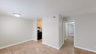 This single-floor residence is designed with a straightforward, functional layout that flows naturally between living, dining, kitchen, and bedroom areas. The main living space is finished with light wood-look laminate flooring and neutral-toned walls, creating a clean, bright atmosphere. A sliding glass door floods the room with natural light and provides direct access to an outdoor balcony area, offering pleasant views of surrounding greenery.

Adjacent to the living area, the kitchen features white cabinetry with decorative paneling, speckled laminate countertops, a double-basin stainless steel sink, and black appliances including a range and dishwasher. The layout provides adequate counter space and storage for everyday use.

A hallway connects the living area to the private sleeping quarters, each of which is finished with plush, neutral-toned carpeting. The bedrooms are well-proportioned, with one room featuring a set of bifold closet doors for built-in storage. The bathroom includes a full-sized soaking tub with an overhead shower, white tile surround, and chrome fixtures, maintaining the unit's consistent, clean aesthetic throughout.

Textured ceilings are present throughout the space, and white baseboards provide a crisp contrast to the neutral wall palette, contributing to a tidy, move-in-ready presentation.