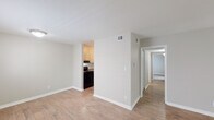 This single-floor residence is designed with a straightforward, functional layout that flows naturally between living, dining, kitchen, and bedroom areas. The main living space is finished with light wood-look laminate flooring and neutral-toned walls, creating a clean, bright atmosphere. A sliding glass door floods the room with natural light and provides direct access to an outdoor balcony area, offering pleasant views of surrounding greenery.

Adjacent to the living area, the kitchen features white cabinetry with decorative paneling, speckled laminate countertops, a double-basin stainless steel sink, and black appliances including a range and dishwasher. The layout provides adequate counter space and storage for everyday use.

A hallway connects the living area to the private sleeping quarters, each of which is finished with plush, neutral-toned carpeting. The bedrooms are well-proportioned, with one room featuring a set of bifold closet doors for built-in storage. The bathroom includes a full-sized soaking tub with an overhead shower, white tile surround, and chrome fixtures, maintaining the unit's consistent, clean aesthetic throughout.

Textured ceilings are present throughout the space, and white baseboards provide a crisp contrast to the neutral wall palette, contributing to a tidy, move-in-ready presentation.