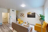 Located at 775 S Belmont St in Delano, CA, this two-story home offers a thoughtfully designed layout spread across two floors. The ground floor hosts an inviting living room with wood-look flooring, a ceiling-mounted light fixture, and a staircase leading to the upper level. Adjacent to the living area is a combined kitchen and dining room, featuring light wood cabinetry, stainless steel appliances including a gas range, microwave, and French door refrigerator, complemented by clean white countertops and recessed lighting. A garage with an automatic opener provides secure parking and interior access. Four bathrooms are distributed throughout the home, including well-appointed spaces with light wood vanities and wood-look flooring. The upper floor contains both bedrooms, including a spacious primary bedroom with plush carpeting, a ceiling fan, a wall-mounted TV, a walk-in closet, and a private en-suite bathroom. The second bedroom also features carpet flooring and a wall-mounted TV. Multiple closets and a dedicated laundry area add to the home's functionality. The overall aesthetic is clean and contemporary, with neutral tones and modern finishes throughout.