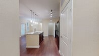 This single-floor residence offers a thoughtfully designed open-concept layout that seamlessly connects the kitchen, dining, and living areas. Rich, dark hardwood flooring flows throughout the main living spaces, creating a warm and cohesive aesthetic.

The kitchen serves as the centerpiece of the home, anchored by a large granite-topped island with a double-basin sink and elegant pendant lighting overhead. Dark espresso cabinetry provides ample storage, while black appliances — including a refrigerator, range, and microwave — complete the functional and stylish setup. Track lighting illuminates the kitchen workspace efficiently.

The open living and dining area benefits from natural light streaming through multiple windows with blinds, and a pendant light fixture adds a finishing touch to the space. The layout provides a generous, flexible footprint ideal for both everyday living and entertaining.

The bedroom features warm hardwood-style flooring, a ceiling fan with light fixture, and a window that invites natural light. A generously sized walk-in closet accompanies the bedroom, outfitted with extensive wire shelving and hanging rods along multiple walls, as well as built-in accessory organizers — offering exceptional storage capacity.

The bathroom includes a soaking tub with tiled surround and built-in corner shelving, finished in clean white tones. Neutral, warm beige walls and white trim throughout the home lend a bright, inviting ambiance.