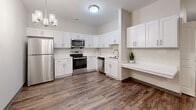Located at 2902 Cozy Court in Evansville, Indiana, this single-story unit offers a thoughtfully designed layout across a comfortable footprint, finished with consistent, contemporary materials throughout. Wood-look luxury vinyl plank flooring runs through every room, providing a warm, cohesive aesthetic that ties the space together.

The kitchen is a standout feature, outfitted with crisp white shaker-style cabinetry, a full suite of stainless steel appliances—including a refrigerator, electric range, built-in microwave, and dishwasher—and a built-in desk or workspace counter along one wall. A multi-light chandelier adds a refined finishing touch overhead.

The bathroom is well-appointed with white cabinetry, a white countertop vanity, a tall storage cabinet, and brushed nickel grab bars, indicating accessibility-conscious design. The bathroom connects to a hallway that leads to the additional rooms.

The remaining rooms feature neutral, light-toned walls with gray baseboard trim, recessed lighting in select areas, and multiple electrical outlets. These versatile spaces can serve a variety of uses. Throughout, the unit presents a clean, move-in-ready condition with a modern, understated aesthetic well-suited for everyday functionality.