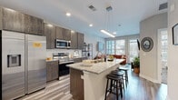 Located at 555 W Fifth Ave in Columbus, Ohio, this single-floor residence offers a thoughtfully designed open-concept layout that seamlessly connects the kitchen, dining, and living areas. The kitchen is a standout feature, showcasing dark wood cabinetry that extends to the ceiling, stainless steel appliances including a full-size refrigerator, electric range, and built-in microwave, all anchored by a granite-topped island with bar seating and a pendant light fixture overhead. Light wood-style flooring runs throughout the main living areas, contributing to a clean, contemporary aesthetic. The living room is generously sized and filled with natural light from large windows and a glass door that opens to a private balcony, offering views of the surrounding urban streetscape. The bedroom is carpeted for comfort and features multiple windows that bring in ample daylight. The bathroom is finished with neutral tile flooring and includes a glass-enclosed shower alongside direct access to a walk-in closet with built-in shelving. Throughout the unit, neutral wall tones and recessed lighting create a bright, modern ambiance well-suited to urban living in the heart of Columbus.
