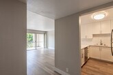 This single-floor unit offers a clean, modern aesthetic throughout its well-organized layout. The living area is spacious and filled with natural light, enhanced by light-toned hardwood flooring and neutral walls that create a bright, airy atmosphere. A sliding glass door opens onto a private balcony, providing outdoor access and views of surrounding greenery.

The kitchen is thoughtfully designed with white shaker-style cabinetry, white quartz countertops, and a classic white subway tile backsplash. Stainless steel appliances — including an electric range, over-the-range microwave, dishwasher, and refrigerator — complete the space. A peninsula counter in one kitchen configuration adds additional workspace and separation from the living area.

The bedroom is carpeted for comfort and features a window that overlooks lush outdoor foliage, offering a calm, private setting. The bathroom includes a single-sink vanity with a large mirror, a toilet, and a tub/shower combination, finished in a simple, functional style with textured walls.

Throughout the unit, clean white baseboards and neutral tones contribute to a cohesive and move-in-ready environment.