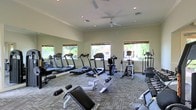 This fitness center offers a comprehensive exercise environment designed to support a wide range of workout routines. The space is outfitted with multiple treadmills, an elliptical trainer, a stationary recumbent bike, and additional cardio equipment, providing ample options for cardiovascular exercise. Strength and flexibility training is supported by a variety of benches and free weights positioned throughout the room.

Large wall-to-wall mirrors line one side of the facility, enhancing the sense of openness and allowing users to monitor their form during workouts. The flooring consists of durable patterned carpet, well-suited for a fitness environment. Recessed lighting provides bright, even illumination throughout the space, while dual ceiling fans promote comfortable air circulation during exercise sessions.

Natural light streams in through multiple windows fitted with woven wood shades, each framing views of lush greenery outside. The overall ambiance is clean, functional, and inviting, striking a balance between practicality and comfort. The single-floor layout ensures easy accessibility and a straightforward, efficient use of space for fitness activities.