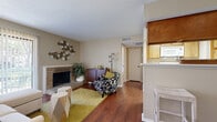 This single-floor residence offers a thoughtfully arranged layout with a warm, inviting ambiance throughout. The living area serves as the heart of the home, anchored by a classic full-height brick fireplace that adds character and charm. Rich hardwood-style flooring flows across the main living spaces, complemented by neutral-toned walls that create a bright, open atmosphere. A large sliding glass door floods the living room with natural light and provides access to an outdoor area, enhancing the sense of openness. The galley-style kitchen is lined with warm wood cabinetry on both sides, offering generous storage, and is equipped with white appliances including a range, built-in microwave, dishwasher, and refrigerator. A double-basin sink and ample counter space make it a highly functional workspace. The bedroom is a serene retreat, featuring plush carpeting, a ceiling fan, and a window that allows for natural light and outdoor views. The full bathroom is finished with hardwood-style flooring, a full-size tub-and-shower combination with clean white tile surround. Textured ceilings are present throughout, adding a distinctive architectural detail that ties the space together cohesively.
