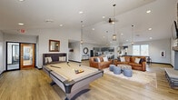 Located on Brook Boulevard in Sandusky, Ohio, this single-floor community clubhouse offers a generously sized, open-concept gathering space designed for both recreation and relaxation. The interior is anchored by soaring vaulted ceilings and light-toned hardwood-style flooring that flows seamlessly throughout, creating a bright and welcoming atmosphere.

The main area serves as a multi-purpose game and lounge room, centered around a full-size pool table and complemented by stylish seating arrangements, including rich leather sofas and accent ottomans arranged on a neutral area rug. A dramatic floor-to-ceiling stacked stone fireplace with a mounted television serves as a striking focal point, adding warmth and character to the space. Decorative wall art and pendant lighting enhance the inviting ambiance.

The kitchen area is well-equipped with gray cabinetry, stainless steel appliances, a large center island with bar seating, and an adjacent dining table — ideal for community gatherings or catered events. Natural light filters in through multiple windows fitted with horizontal blinds.

Additional features include a casual dining nook near an exterior door with outdoor views, and two ADA-accessible restrooms finished with large-format gray tile, stainless steel grab bars, and clean, modern fixtures. The space is thoughtfully designed to serve a diverse community with both comfort and accessibility in mind.