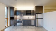 Located in Portland's vibrant NW District, this contemporary single-floor unit at 1315 NW 19th Ave offers a thoughtfully designed layout with a clean, modern aesthetic. Polished concrete floors run throughout the space, lending an industrial-chic character that complements the overall design.

The kitchen is a standout feature, outfitted with dark espresso cabinetry, a white tile backsplash, and a full suite of stainless steel appliances including an electric range, dishwasher, and refrigerator. Tall upper cabinets maximize storage, while under-cabinet lighting adds a warm, practical glow. Large wood-framed windows beside the kitchen bring in natural light and offer views of the surrounding neighborhood.

A clean, well-lit hallway connects the main living area to the bathroom and additional spaces. The living area is bright and open, with white walls, a wall-mounted HVAC unit, and a window that fills the room with natural light — providing a versatile, move-in-ready canvas.

The bathroom continues the modern design language with dark wood cabinetry, a single-sink vanity, a full soaking tub with shower, and recessed lighting set against crisp white walls and concrete flooring. The space is efficiently organized and well-appointed throughout.