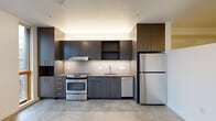 Located in Portland's vibrant NW District, this contemporary single-floor unit at 1315 NW 19th Ave offers a thoughtfully designed layout with a clean, modern aesthetic. Polished concrete floors run throughout the space, lending an industrial-chic character that complements the overall design.

The kitchen is a standout feature, outfitted with dark espresso cabinetry, a white tile backsplash, and a full suite of stainless steel appliances including an electric range, dishwasher, and refrigerator. Tall upper cabinets maximize storage, while under-cabinet lighting adds a warm, practical glow. Large wood-framed windows beside the kitchen bring in natural light and offer views of the surrounding neighborhood.

A clean, well-lit hallway connects the main living area to the bathroom and additional spaces. The living area is bright and open, with white walls, a wall-mounted HVAC unit, and a window that fills the room with natural light — providing a versatile, move-in-ready canvas.

The bathroom continues the modern design language with dark wood cabinetry, a single-sink vanity, a full soaking tub with shower, and recessed lighting set against crisp white walls and concrete flooring. The space is efficiently organized and well-appointed throughout.